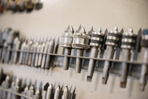 A large range of metal tools and machining bits are arranged in a row on a wall.