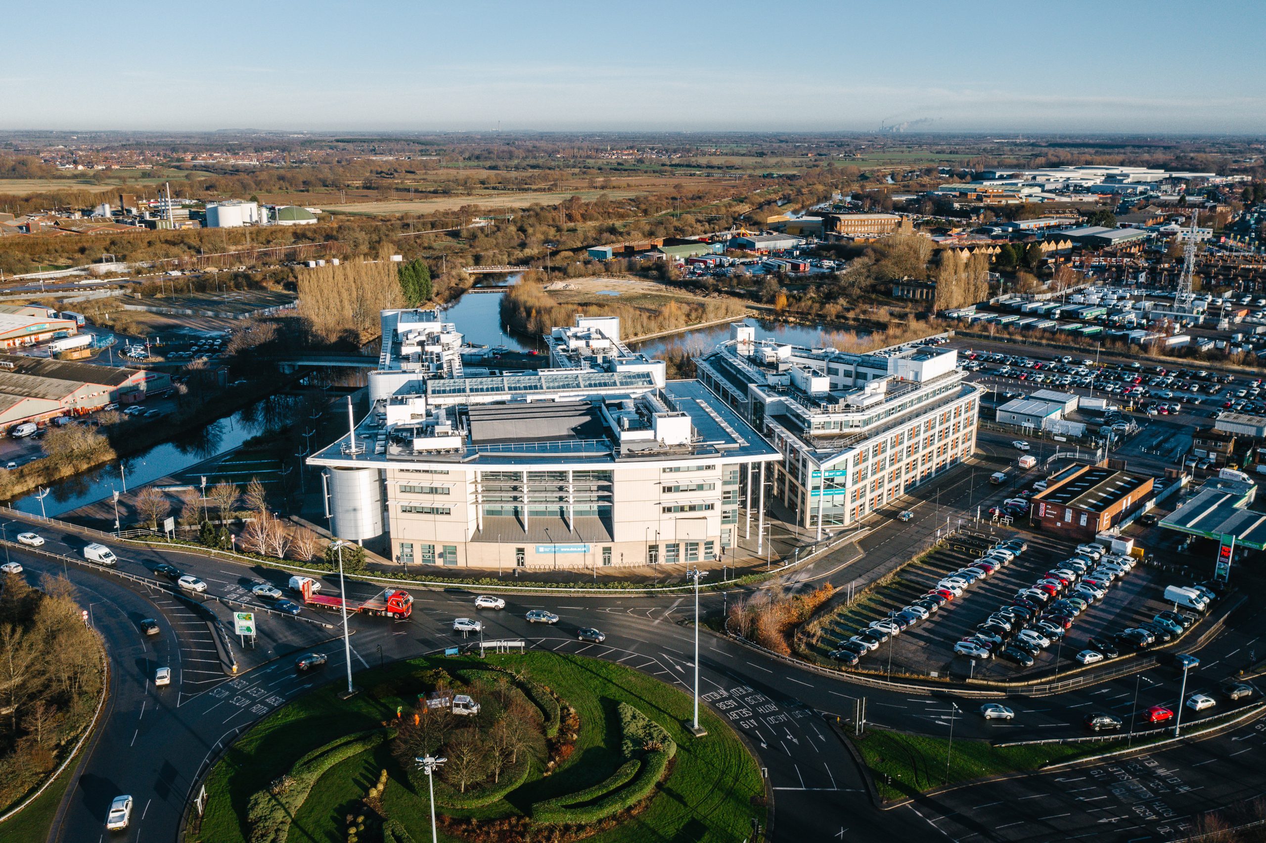 Aerial view of Doncaster College, featuring modern buildings, a nearby waterway, and a busy roundabout with cars, surrounded by urban and rural landscapes.