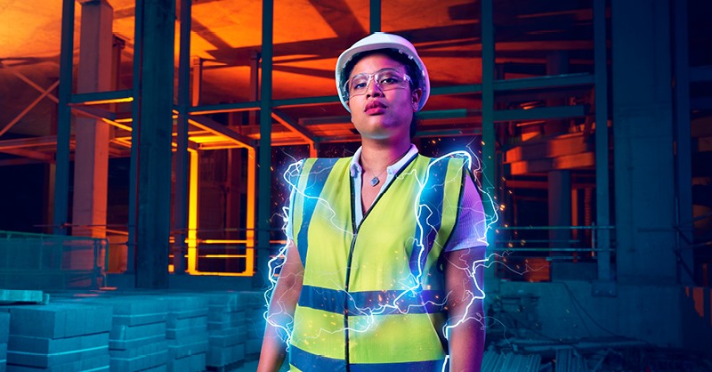 A stylised image showing a person in a high visibilty jacket and hard hat, with added lighting graphics around their arms. They are in a dark orange-lit construction setting.